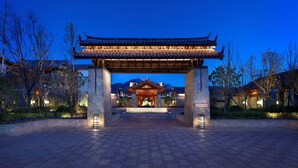 A traditional Chinese-style building entrance with a tiled roof and stone pillars, surrounded by landscaped gardens and a mountainous backdrop. - Jinmao Purelax Lijiang -The Unbound Collection by Hyatt (Lijiang)