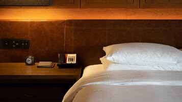 Una habitación de hotel con una cama, una mesita de noche con un reloj, un control remoto y una alfombra estampada.