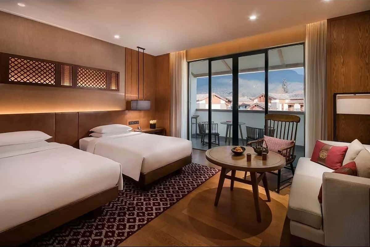 Ein Hotelzimmer mit zwei Betten, einem Esstisch, einem Balkon mit Blick auf Gebäude und einem Sofa.
