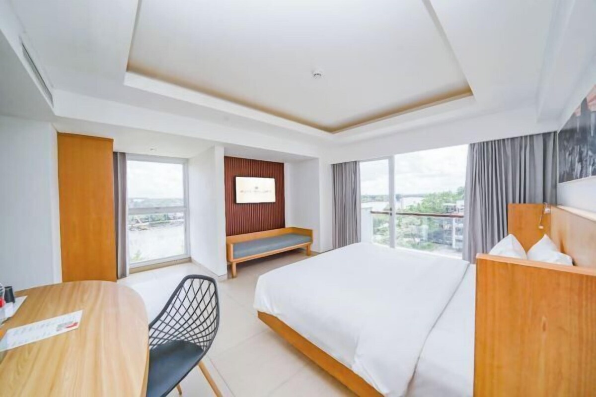 Habitación de hotel con cama, escritorio, silla, televisión y vista a la ciudad.