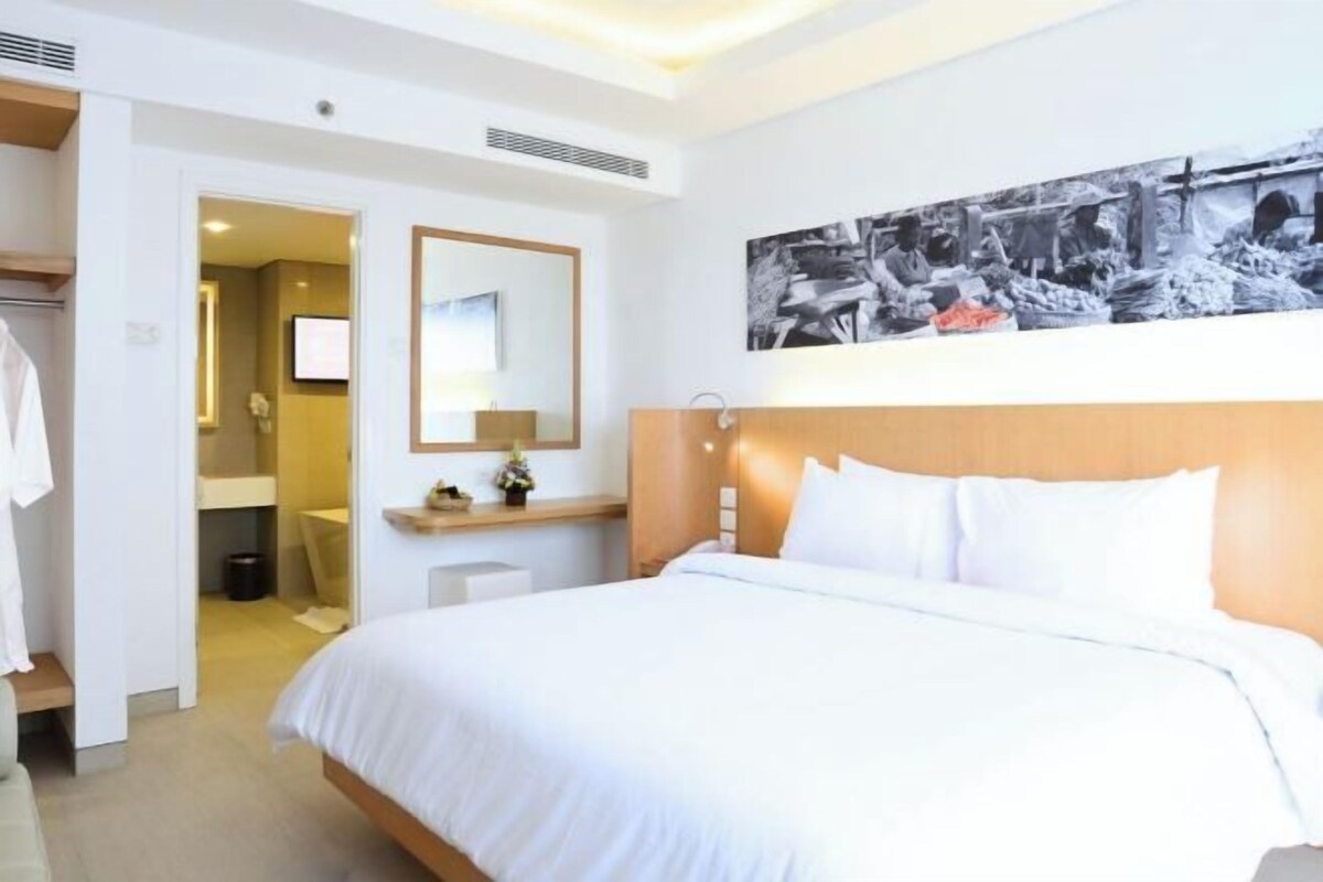 Una habitación de hotel con cama, espejo, una obra de arte en la pared y televisor.