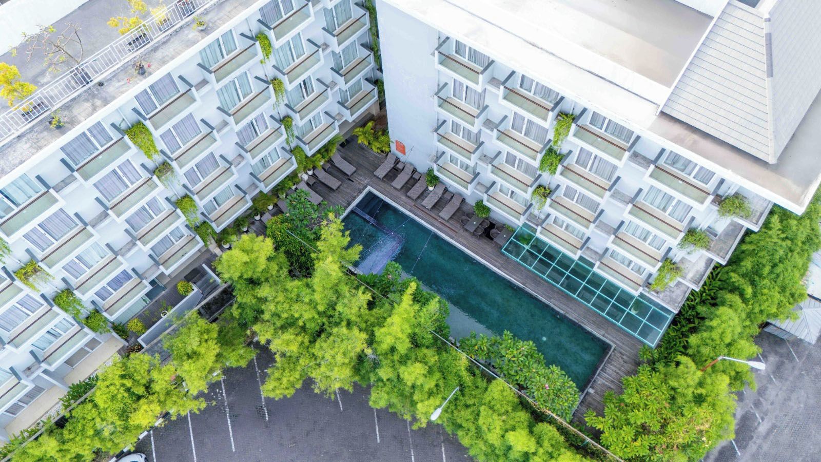 Un hotel de varios pisos con balcones, piscina y follaje circundante.