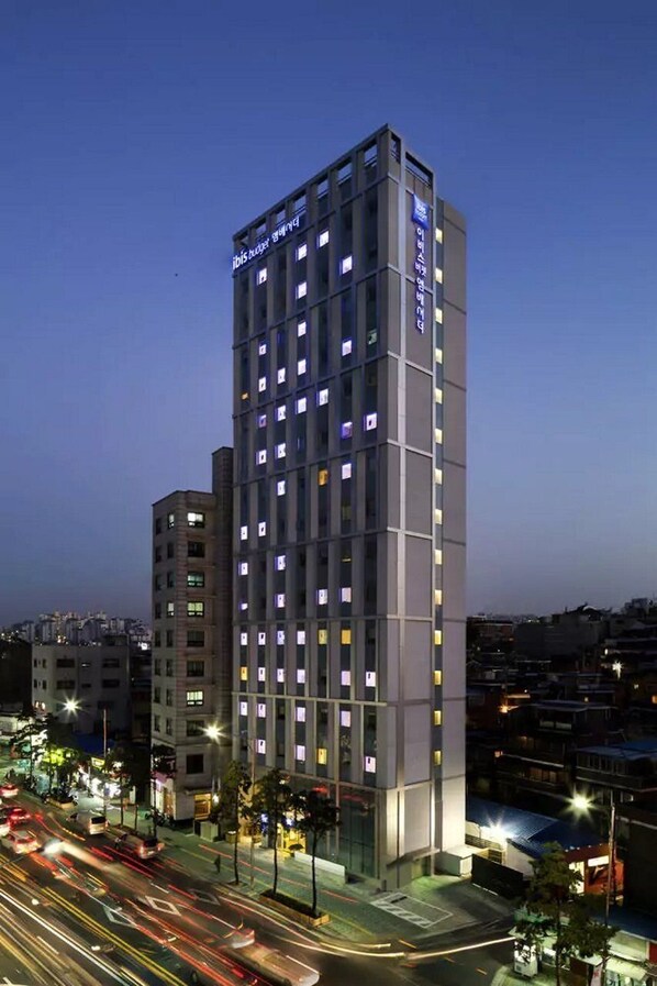 Un hotel de varios pisos con un diseño moderno, que destaca por una entrada imponente y una serie de ventanas en cada planta.