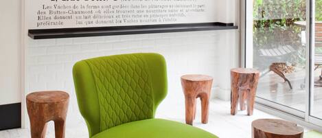 A modern room with a green cushioned chair, wooden stools, and a magazine on a table.