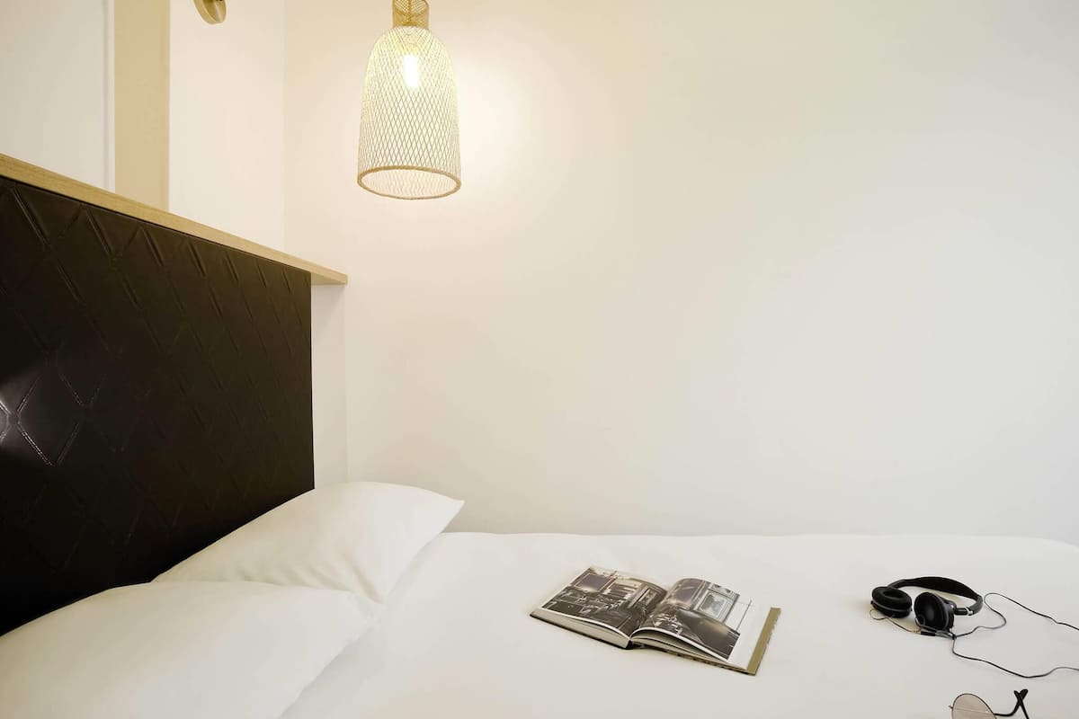 A neatly made bed with a book, headphones, and glasses on it.