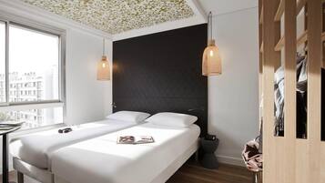 Un dormitorio moderno con una cama grande, dos lámparas colgantes, un cabecero negro y vistas de la ciudad a través de una ventana.
