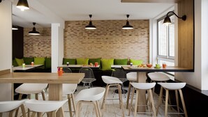 A modern cafe with brick walls, wooden tables, and green cushioned seating. - ibis Styles Paris Buttes Chaumont (Paris)