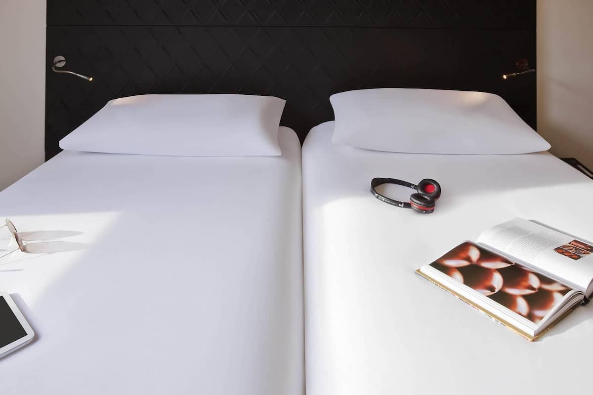 A hotel room with two beds, a black headboard, a book, and a pair of headphones on one bed.