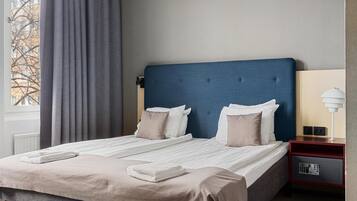 Una habitación de hotel con una cama grande, una mesita de noche con lámpara y vistas a árboles.