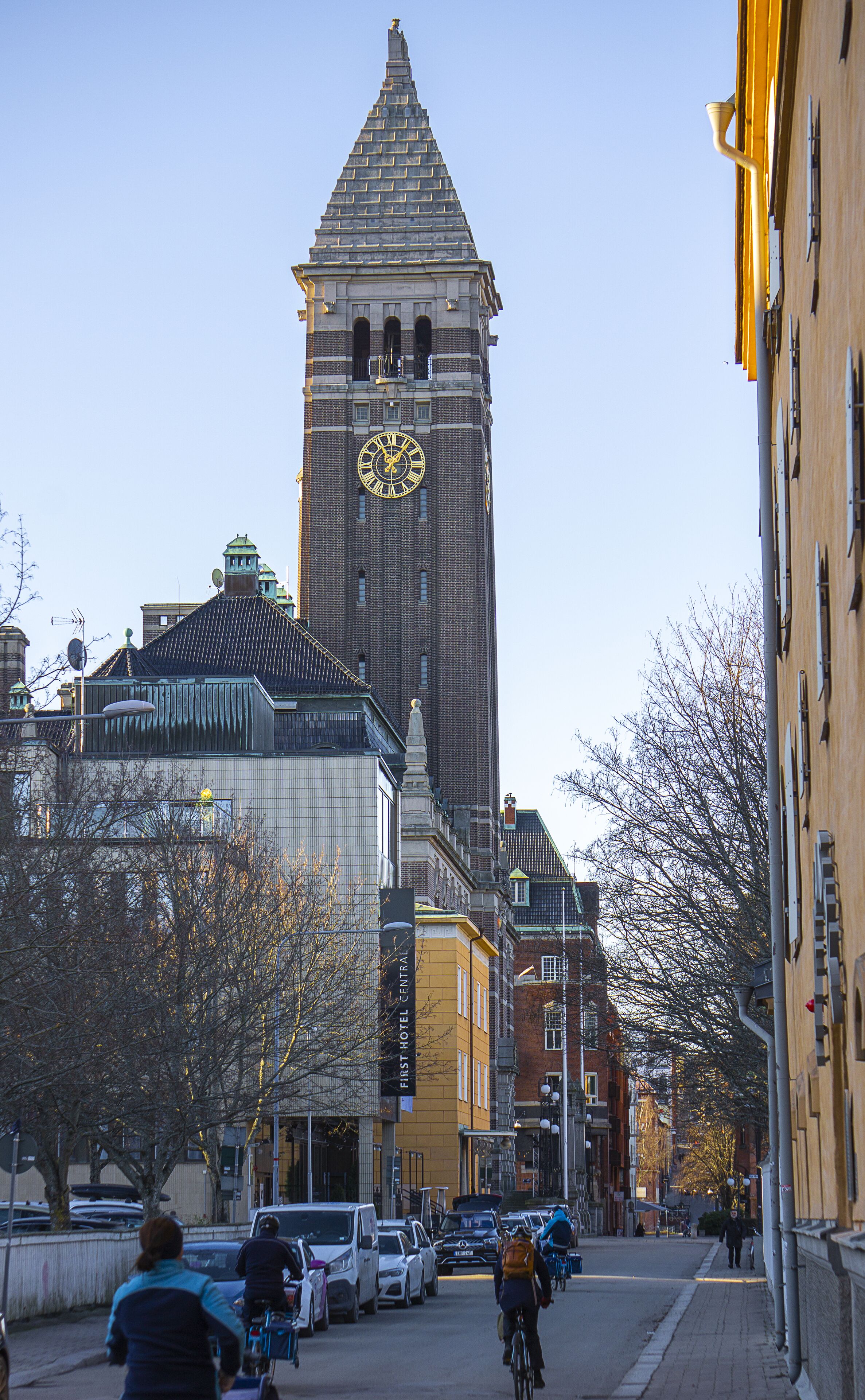 Una histórica torre del reloj de diseño clásico, rodeada de edificios urbanos y un cielo despejado.
