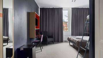 Habitación de hotel pequeña con cama, escritorio, silla, armario y ventana con cortinas.