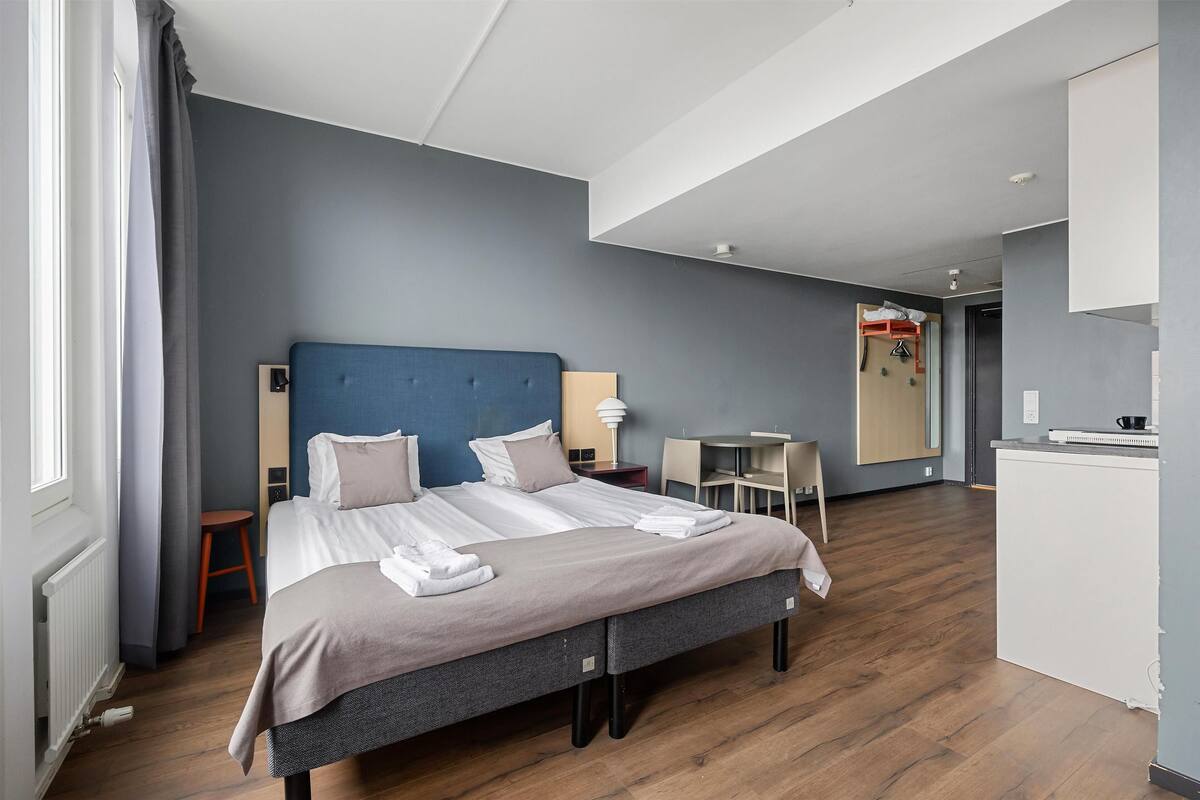 A modern hotel room with a large bed, a desk, and a small seating area.
