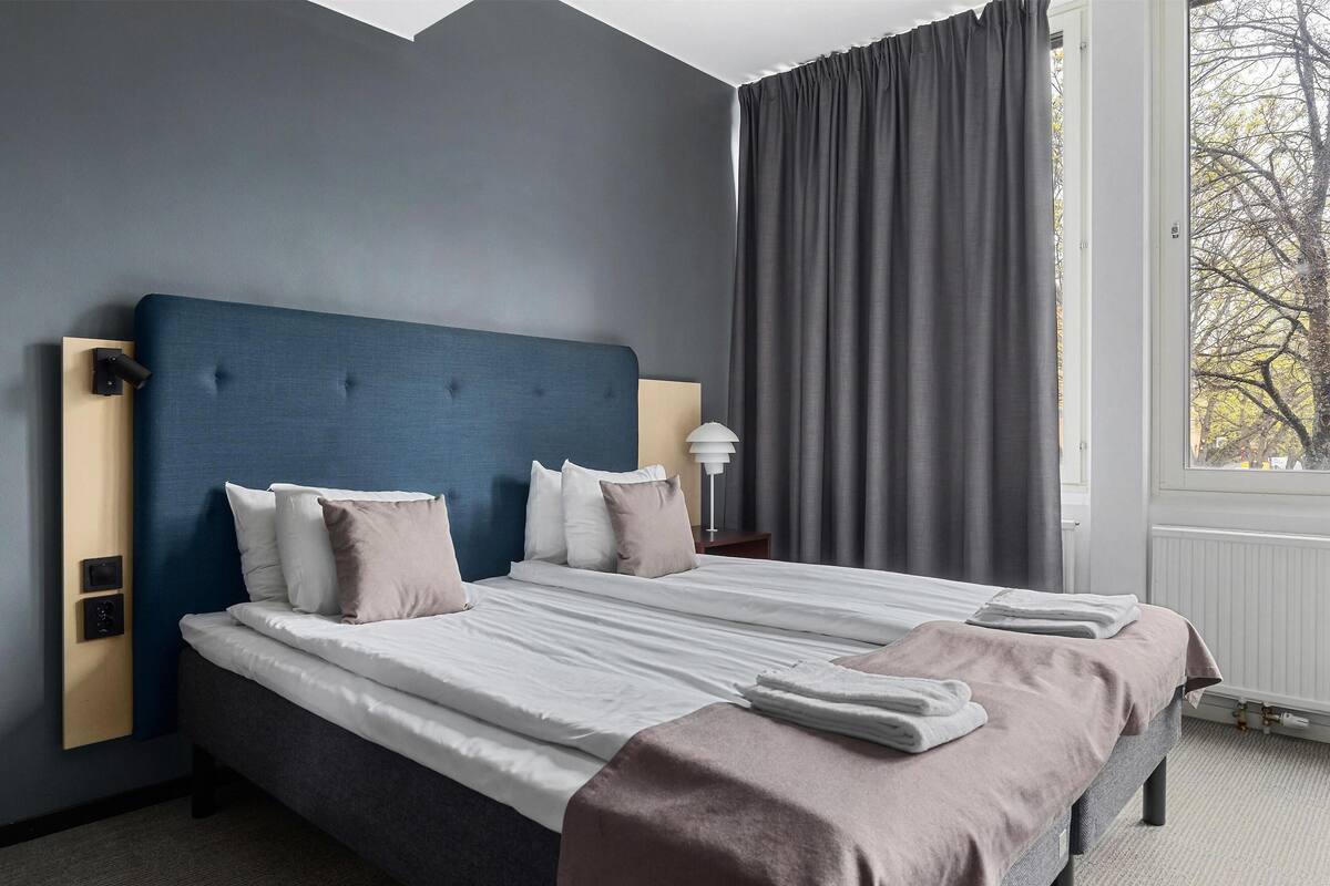 A neatly made bed with pillows, a bedside lamp, and a window with curtains.