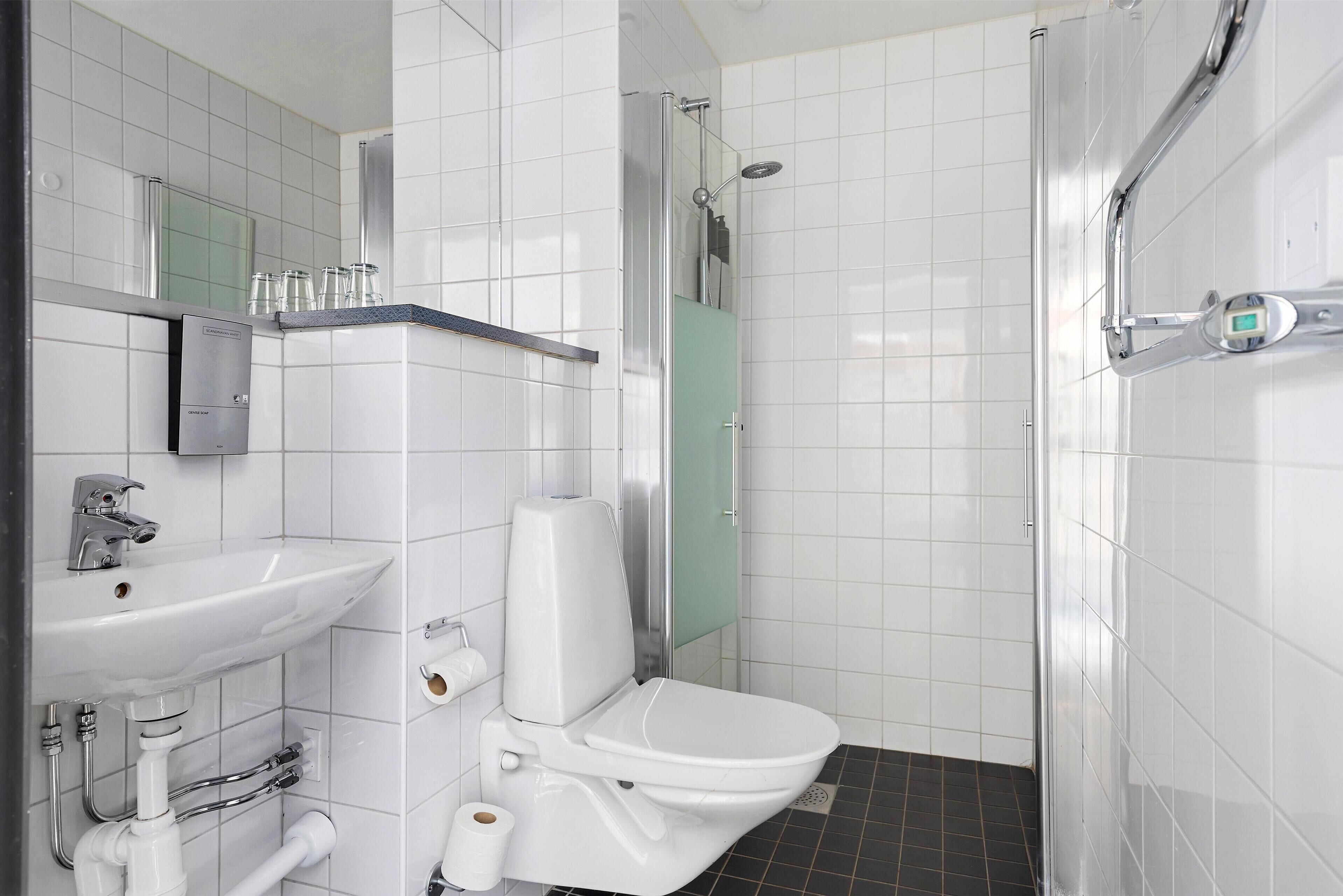 Une salle de bain moderne avec un lavabo, des toilettes et une douche, le tout de couleur blanche.