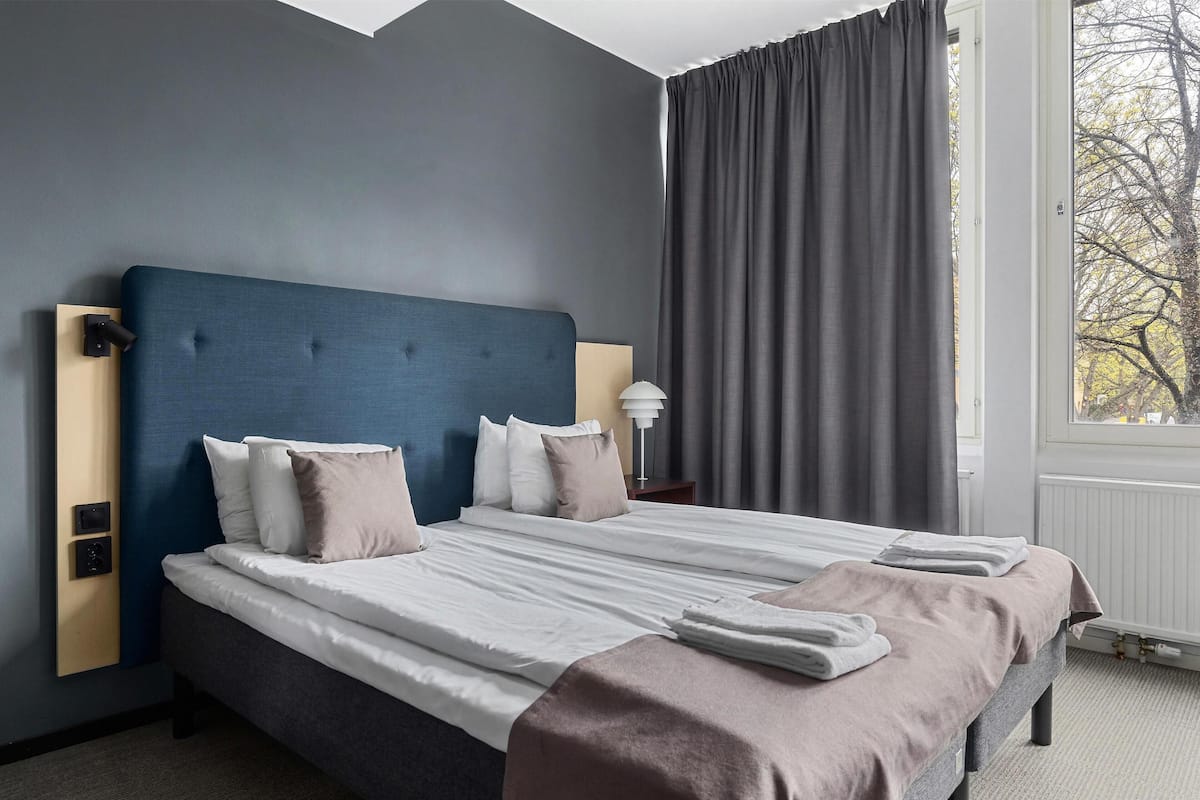 A neatly made bed with a blue headboard, white and beige pillows, and a brown throw blanket.