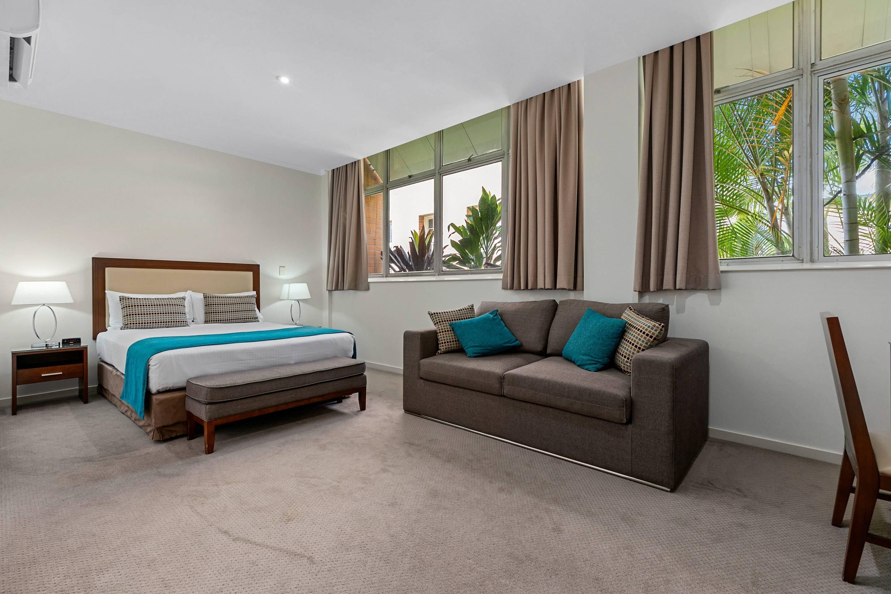 Un dormitorio con cama, mesitas de noche, un sofá y una ventana con cortinas.