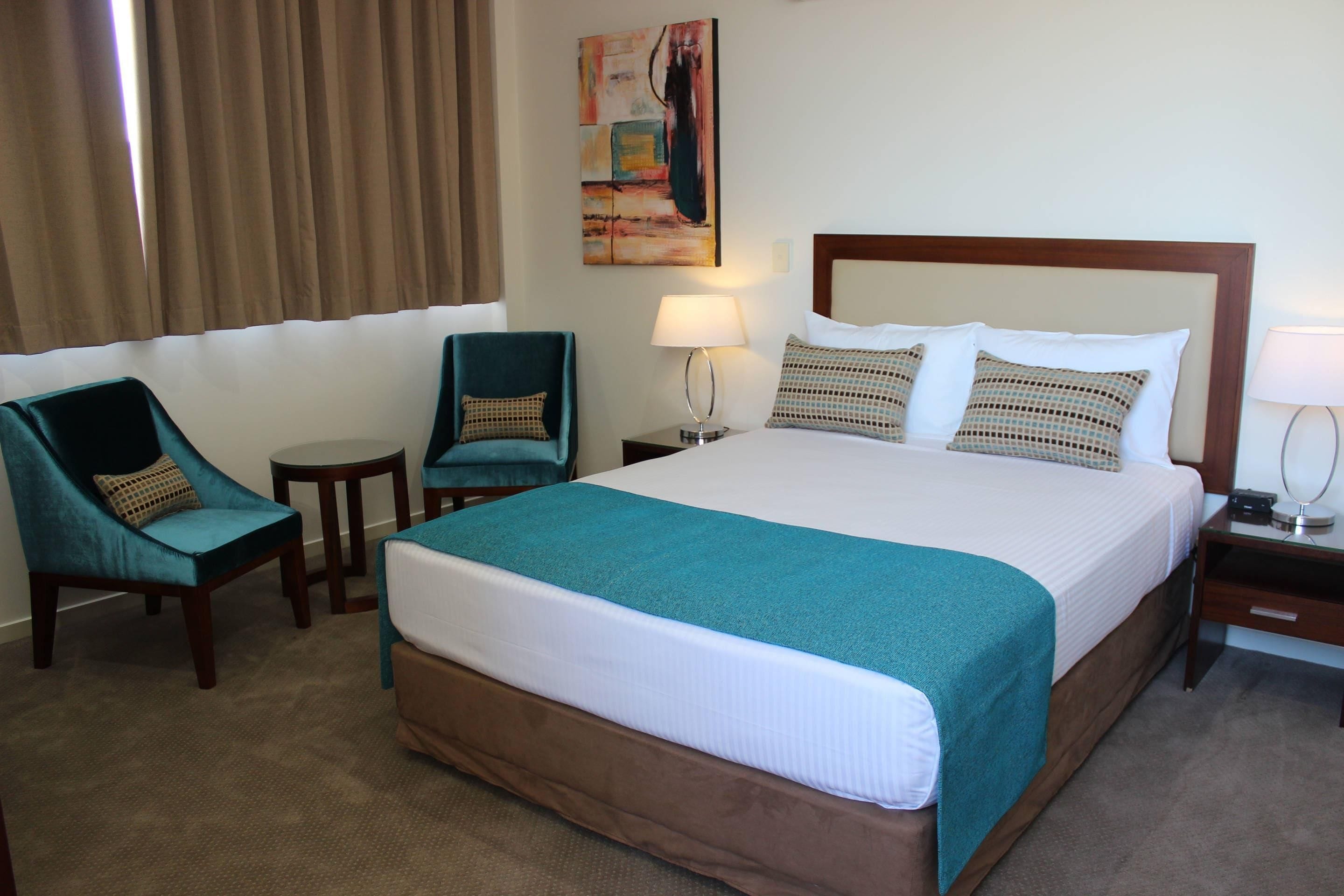Een hotelkamer met een groot bed, twee fauteuils, een tafeltje en een nachtkastje met een lamp.
