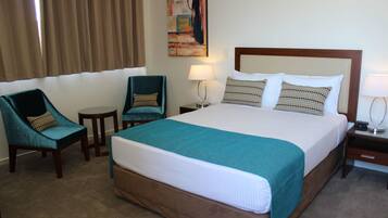 Een hotelkamer met een groot bed, twee fauteuils, een tafeltje en een nachtkastje met een lamp.