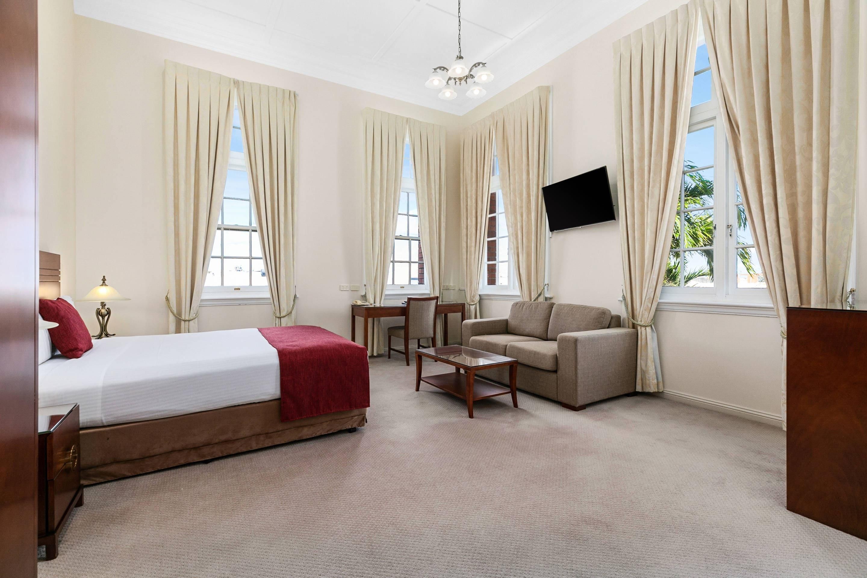 A hotel room with a bed, a sofa, a small table, and a TV mounted on the wall.