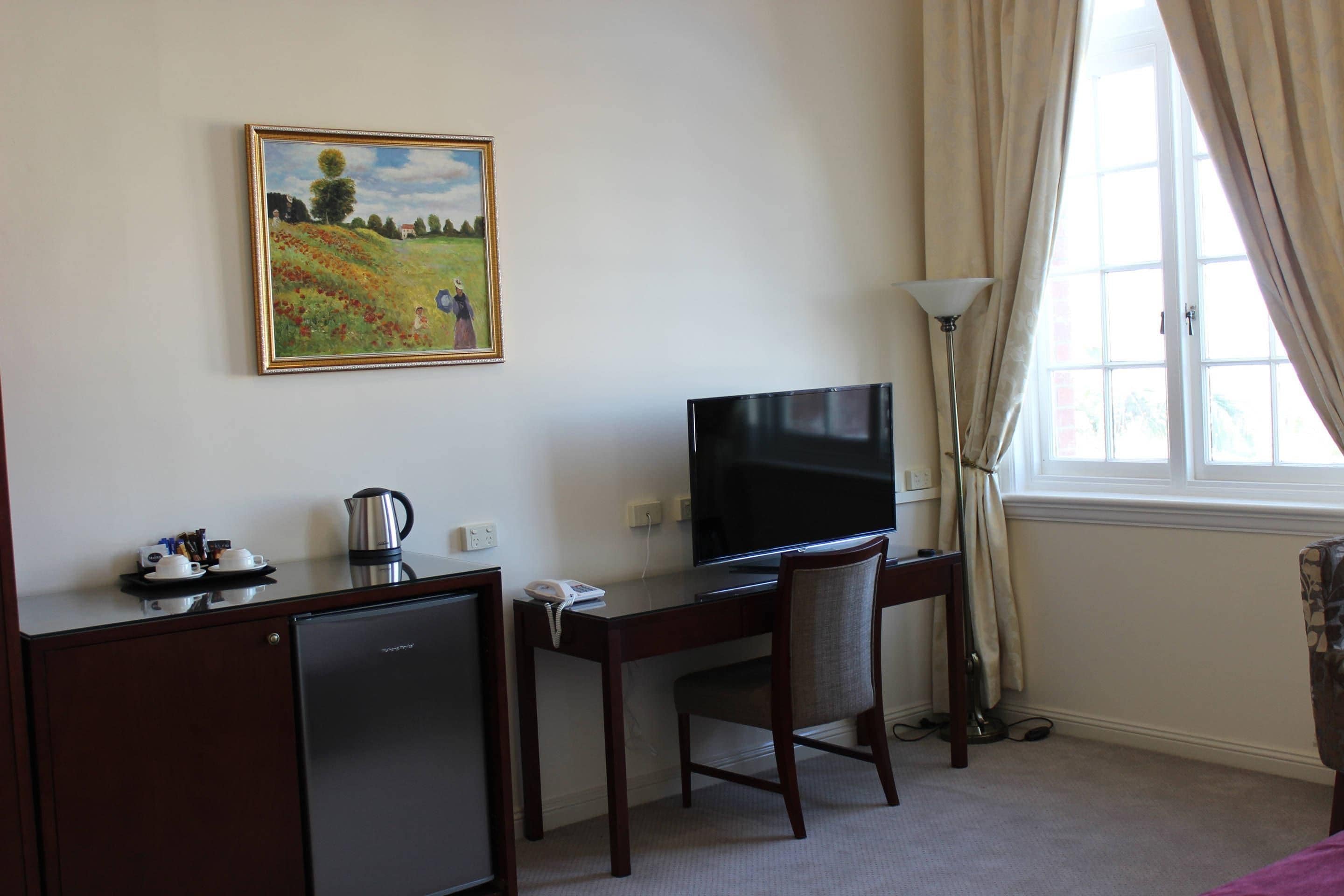 Une chambre d’hôtel équipée d’un bureau, d’une télévision et d’un petit réfrigérateur.