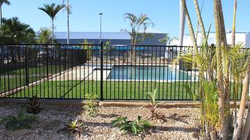 Un área exterior cercada con piscina, rodeada de palmeras y un edificio al fondo.