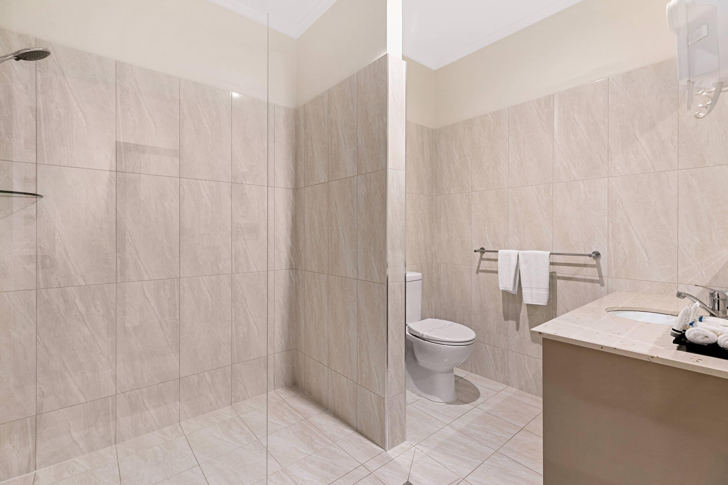 Un baño moderno con ducha envuelta en vidrio, inodoro y tocador con lavamanos y toallero.