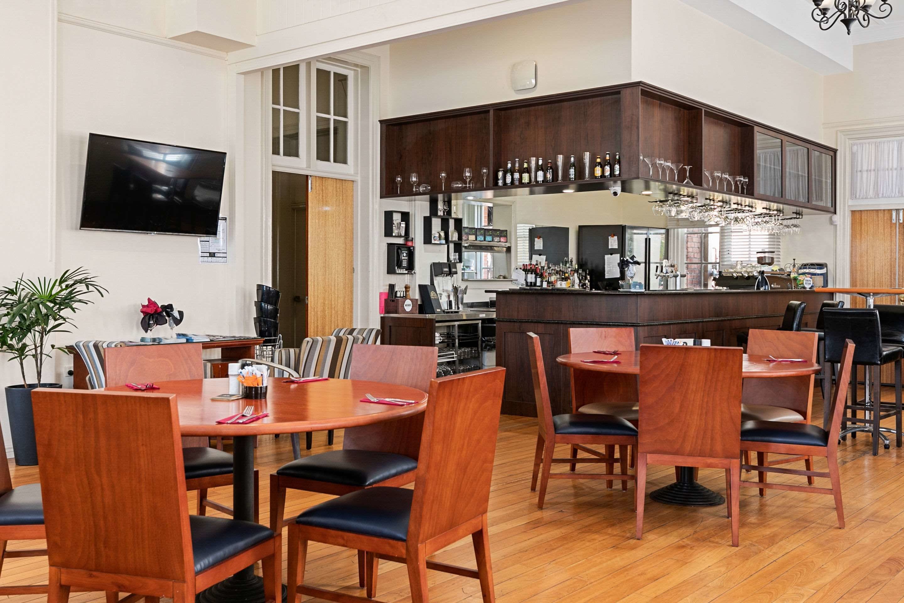 A spacious dining area with wooden tables and chairs, a kitchen with a bar, and a TV mounted on the wall.