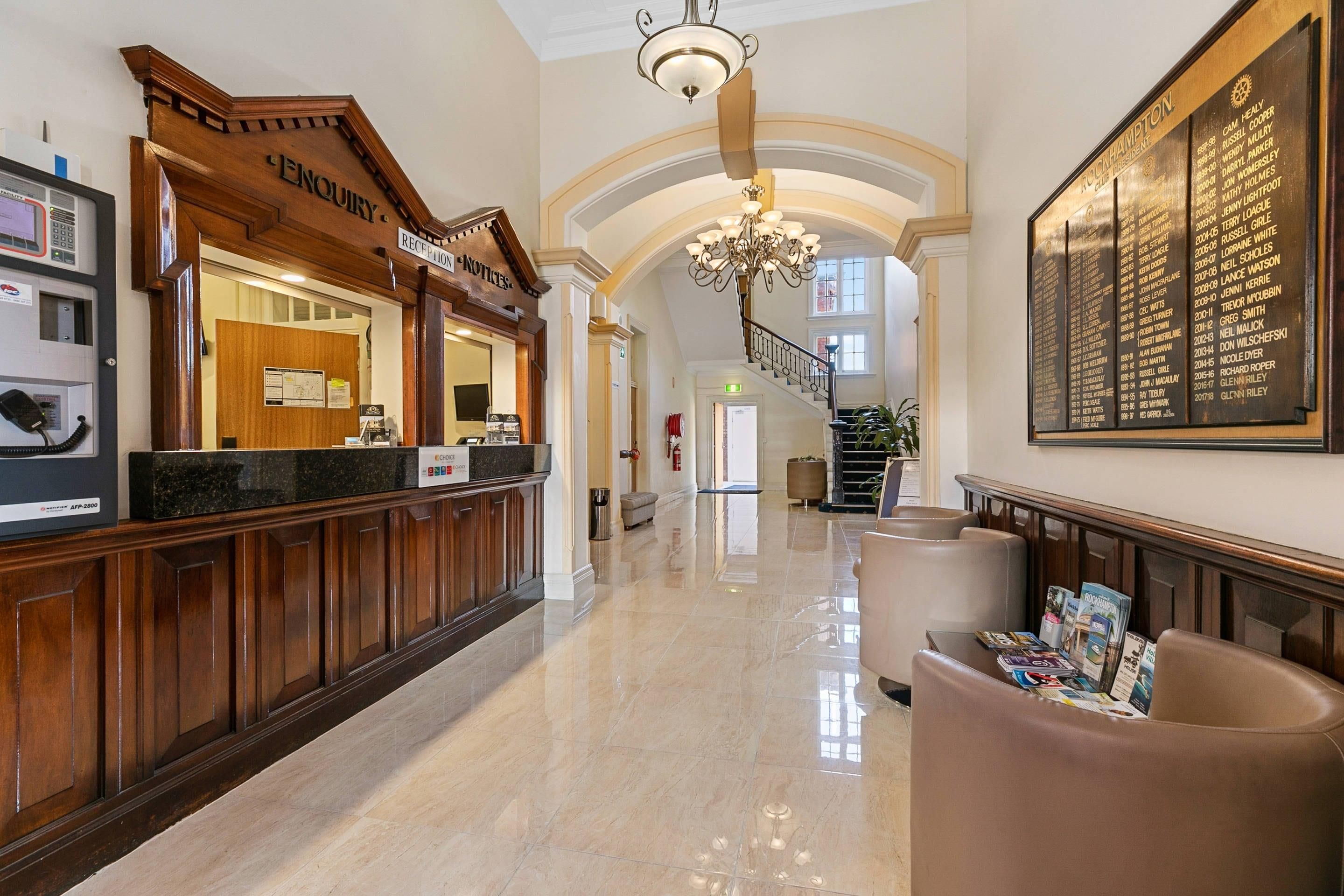 A reception area with a reception desk, a chandelier, a staircase, and a wall with a list of names.