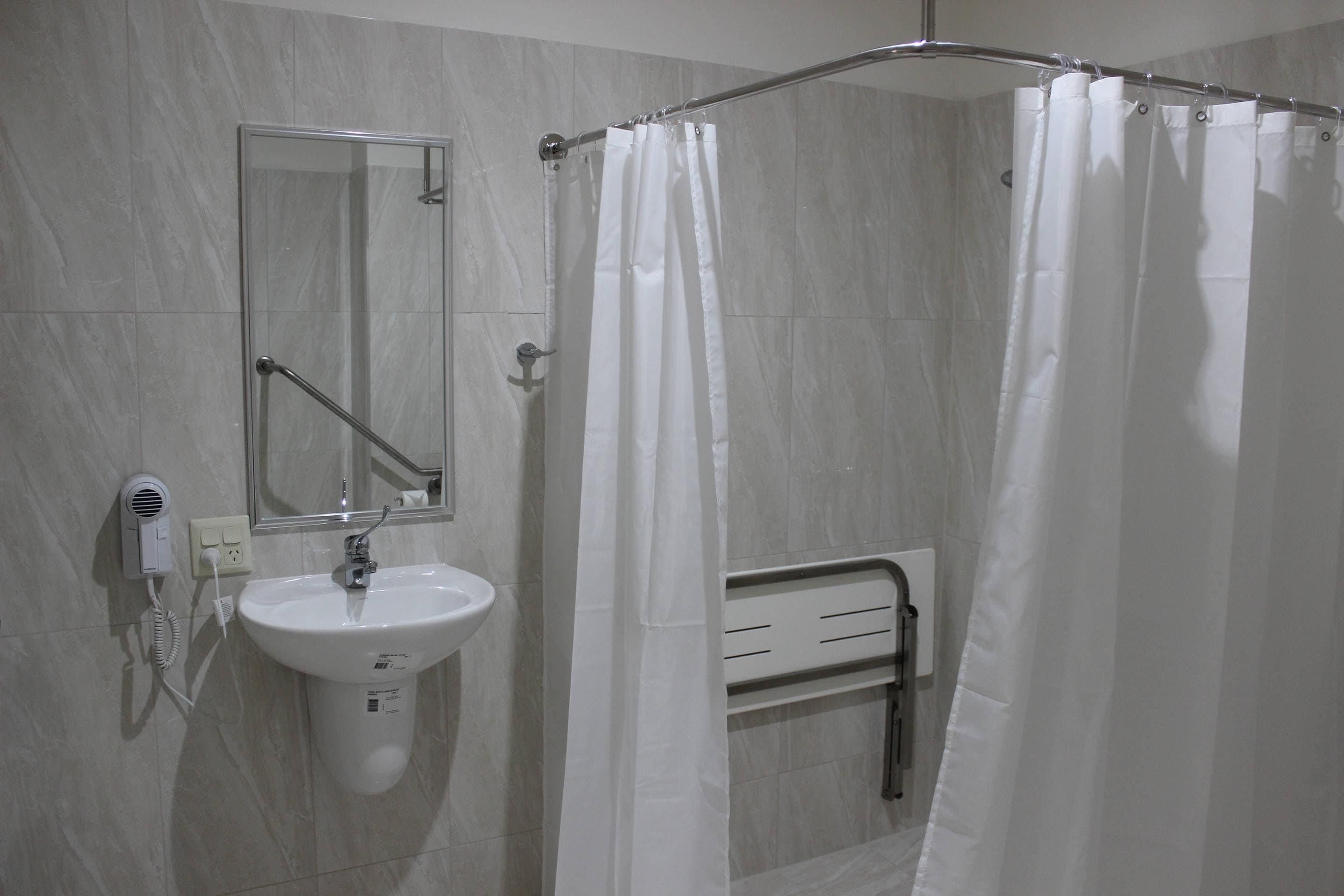 A bathroom with a white sink, a mirror, a shower curtain, and a towel rack.