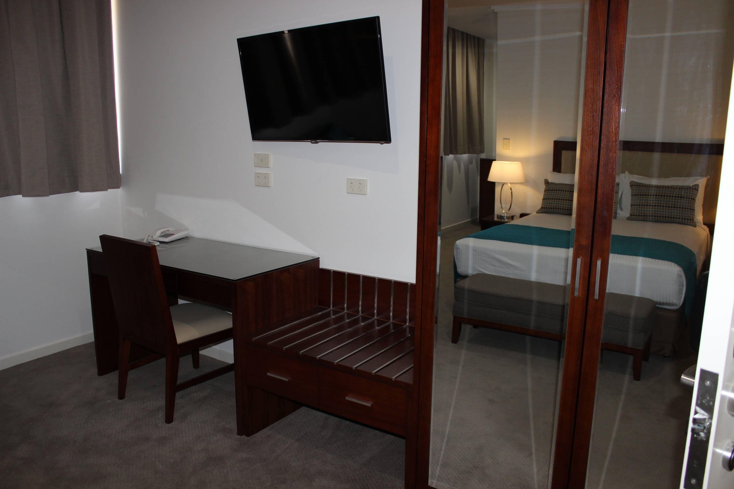 Ein Hotelzimmer mit Schreibtisch, Stuhl, Fernseher, Bett und Spiegel.