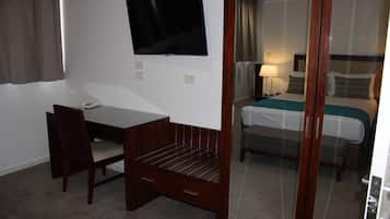 Ein Hotelzimmer mit Schreibtisch, Stuhl, Fernseher, Bett und Spiegel.