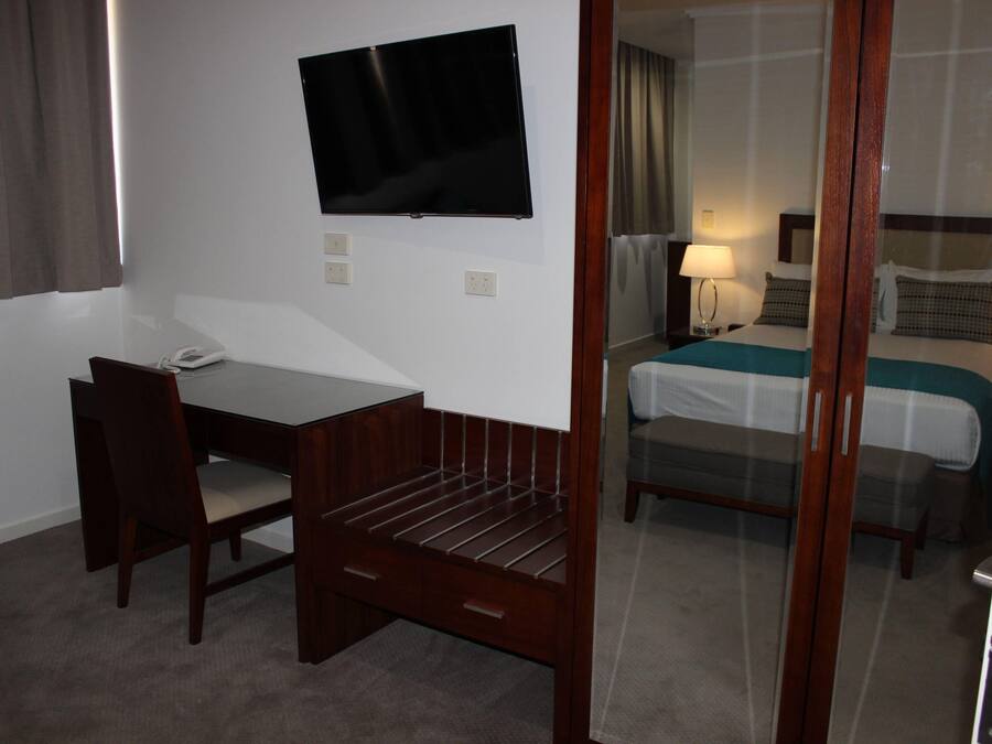 Ein Hotelzimmer mit Schreibtisch, Stuhl, Fernseher, Bett und Spiegel.