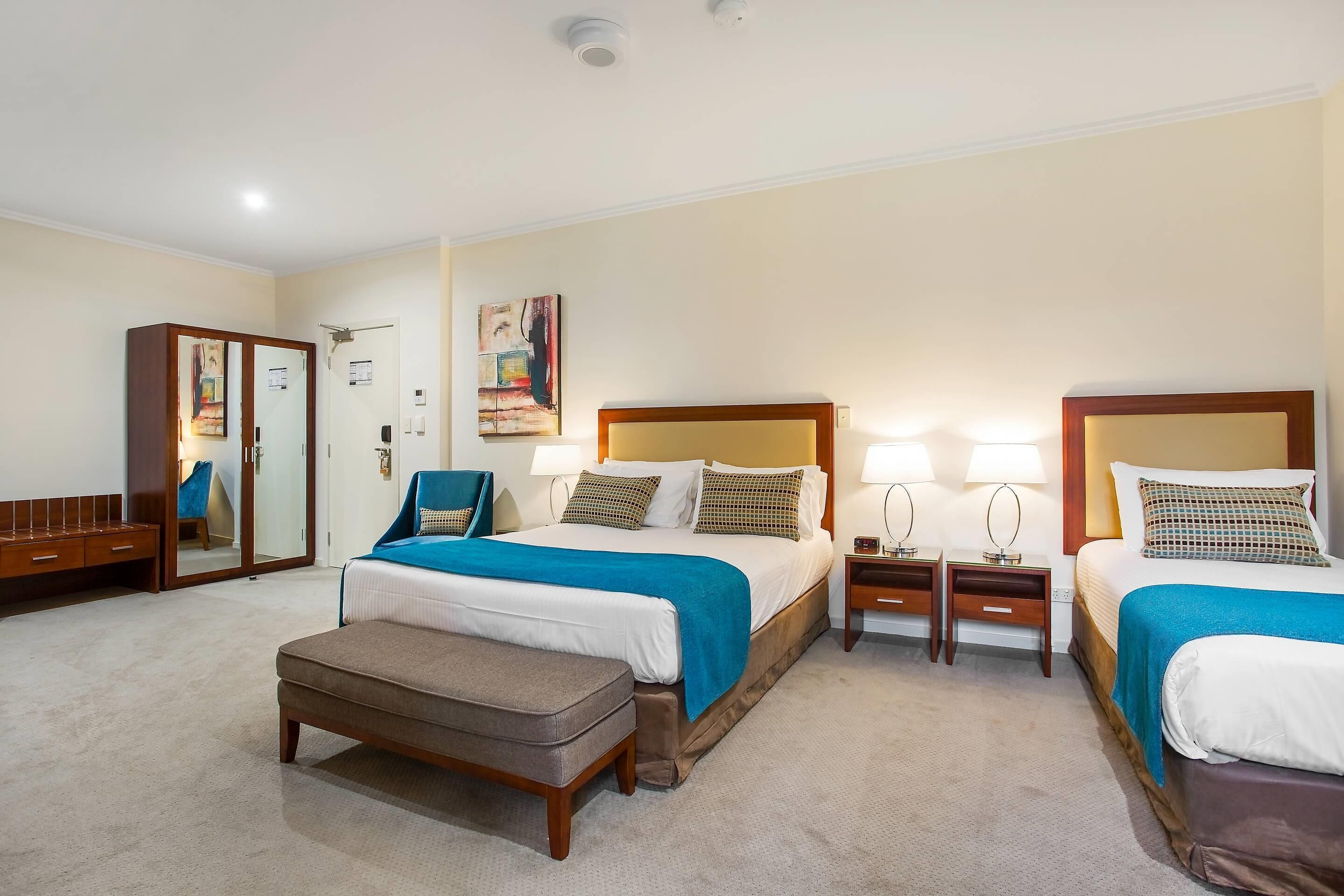 A hotel room with a large bed, two bedside tables, a chair, a wardrobe, and a mirror.