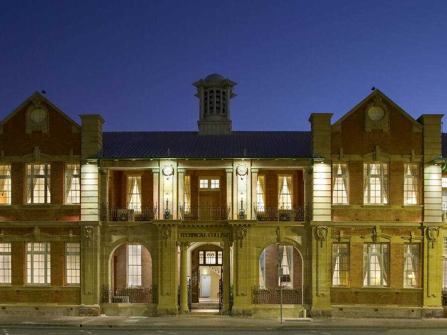 Un edificio grande e histórico de varias plantas, con ventanas de arco y una entrada central que dice "Technical College".