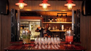 Zona de bar con mostrador de madera, varios vasos de vino y un refrigerador lleno de botellas.