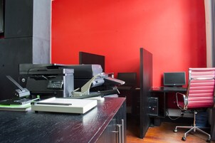 A modern office with a red wall, a black desk, a printer, a computer, and a red office chair.