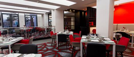 A modern dining area with tables set for four, red and black chairs, and a red accent wall.