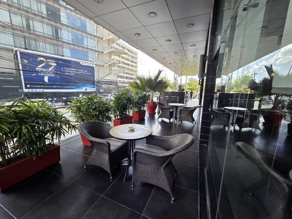 An outdoor seating area with wicker chairs and tables, surrounded by potted plants. - Onomo Hotel Dar es Salaam (Dar es Salaam)