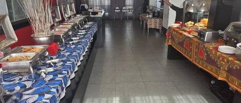 Een buffetopstelling met verschillende thematafels en een eetgedeelte met tafels en stoelen.
