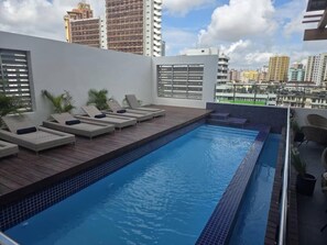 Piscina en la azotea con sillones de descanso y vistas a la ciudad.