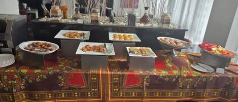 A buffet table with various food items and a decorative tablecloth.