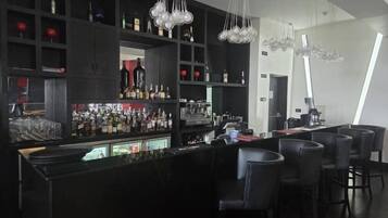 Un área de bar moderna con estantes negros llenos de botellas, una barra y taburetes negros.
