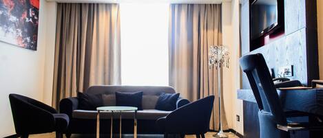 A modern living room with a sofa, two armchairs, a coffee table, and a TV mounted on the wall.