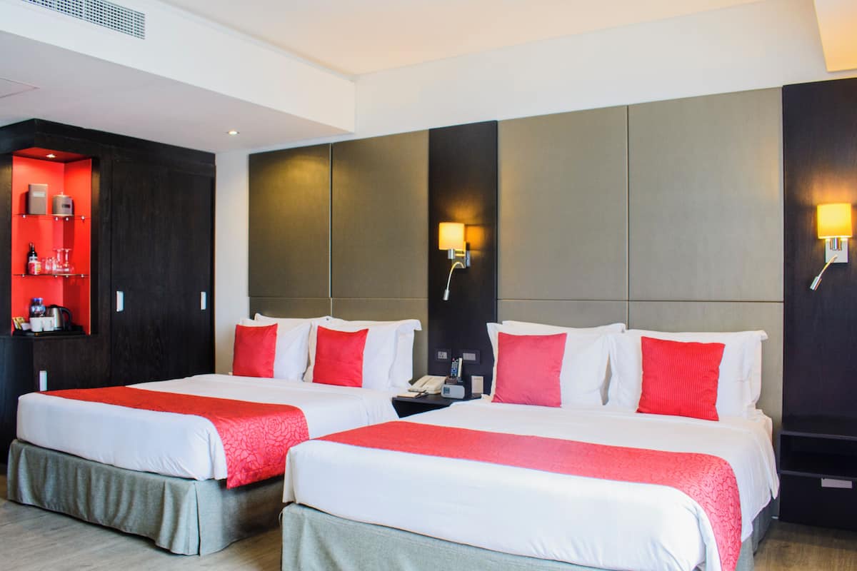 Habitación de hotel con dos camas, cada una con ropa de cama blanca y roja, un minibar y lámparas fijadas a la pared.