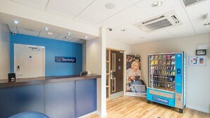 Een receptiegedeelte met een blauwe muur, een Travelodge bord, een automaat en een poster.