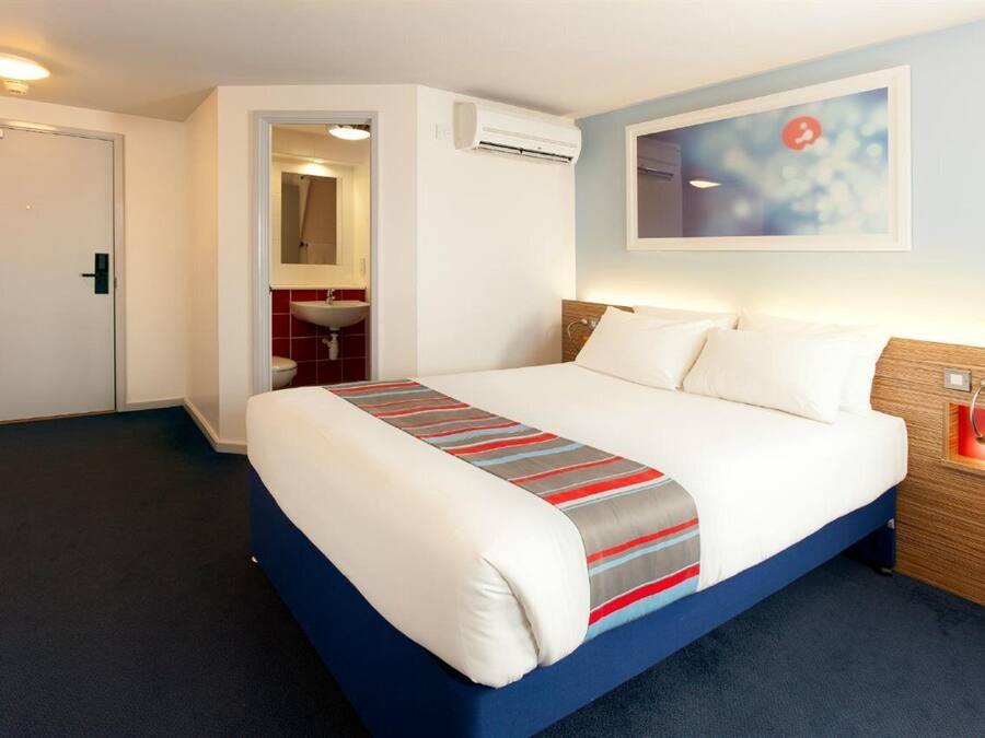 A hotel room with a bed, a bathroom, and a wall-mounted air conditioning unit.