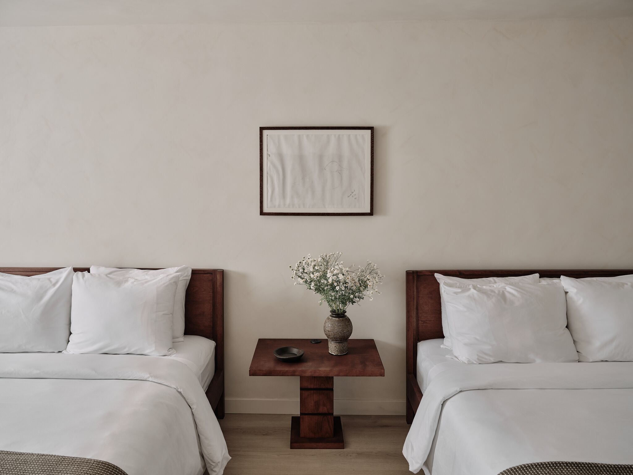Ein Hotelzimmer mit zwei Betten, einem kleinen Tisch mit Blumenvase und einem gerahmten Bild an der Wand.