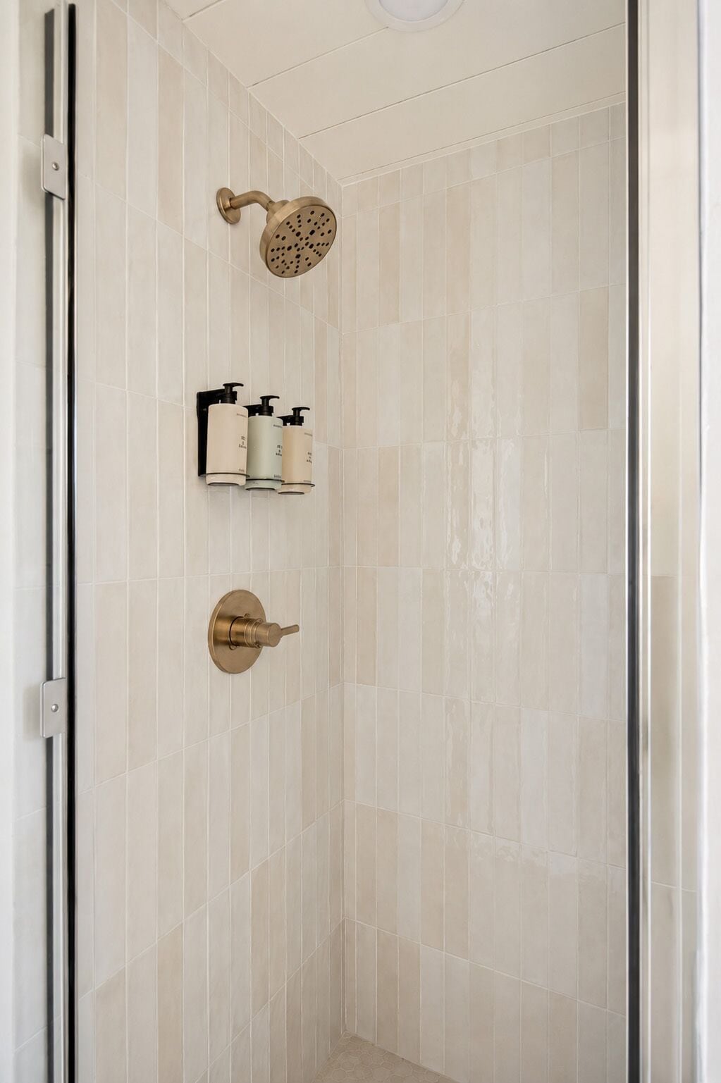 A shower with a handheld showerhead, a wall-mounted soap dispenser, and a door handle.