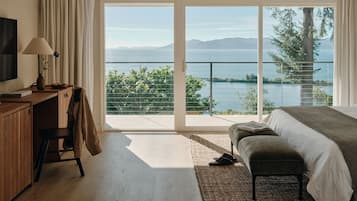 A bedroom with a large sliding glass door leading to a balcony with a view of a lake and mountains.