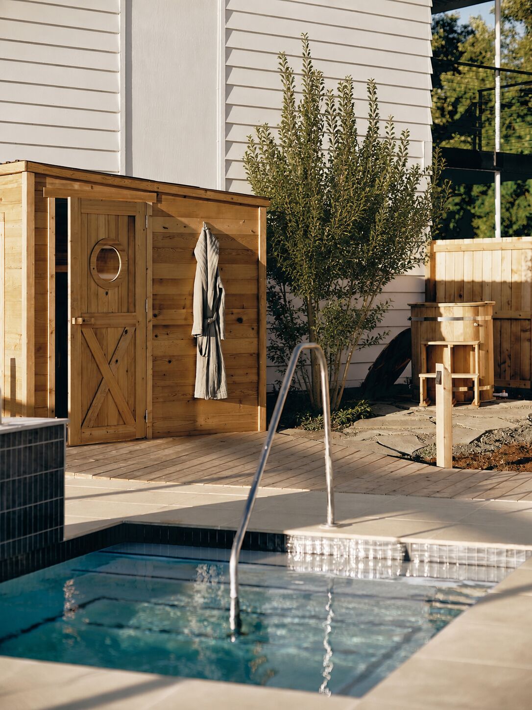 A wooden sauna structure with a door and towel rack, adjacent to a swimming pool with a metal ladder.